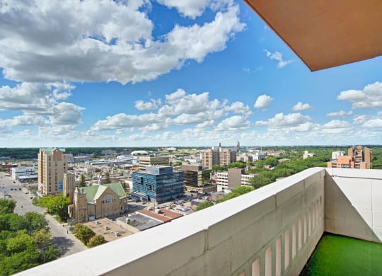 Aerial view of a cityscape from Marquis Towers Apartment Homes, featuring diverse buildings and a historic church. Fluffy clouds and a bright blue sky create a serene atmosphere.