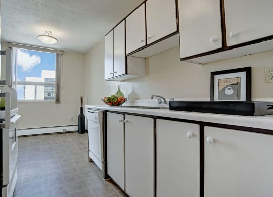 Bright kitchen here at Marquis Towers Apartment Homes with white cabinets, a large window letting in natural light, and fruit bowl on counter. Modern, clean, and minimalistic feel.