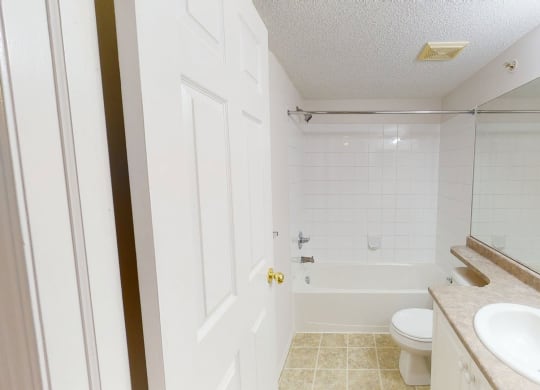 Bright bathroom here at The Pointe at Applewood with white tiles, a bathtub with shower, beige countertop with a sink, and a toilet. A serene and clean atmosphere.