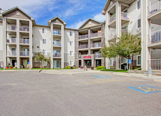 Four-story The Pointe at Applewood apartment building with light-colored siding and stone accents. Balconies line the front, surrounded by trees and accessible parking. Bright, clear day.
