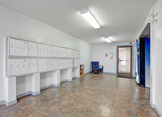 Bright, clean lobby here at Westhaven Estates Apartment Homes with white mailboxes on the left, a blue chair and small bookshelf to the right, and a vending machine near the entrance.