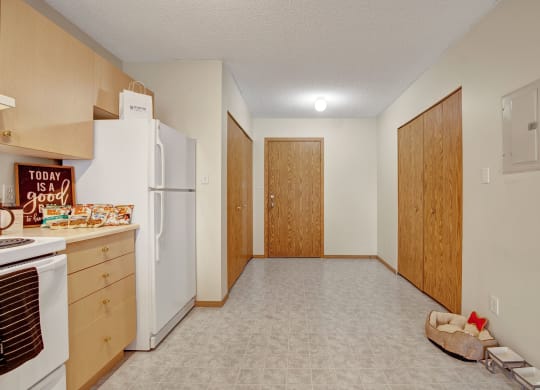 A cozy kitchen here at Westhaven Estates Apartment Homes with wooden cabinets, a white refrigerator, and a “Today is a good day” sign. A dog bed and bowls sit on the floor, adding warmth.