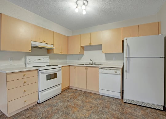 Simple kitchen here at Westhaven Estates Apartment Homes with light wood cabinets, white appliances including a stove, fridge, and dishwasher. Neutral tone, clean and organized space.
