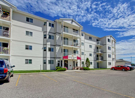 Four-story white Westhaven Estates Apartment Homes building under a vibrant blue sky with scattered clouds. The entrance has a maroon awning and there are parked cars in front.
