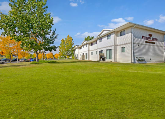 Apartment building labeled "Westhaven Estates" with white exterior, surrounded by green lawn, trees with autumn leaves, and bright blue sky.