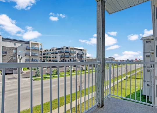 View from a balcony here at Windsor Terrace Apartment Homes showing a modern apartment complex across the street under a clear blue sky. The scene feels open and airy, with neatly trimmed grass.