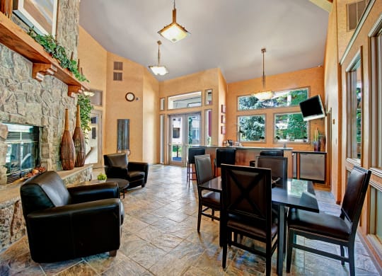 Modern room here at Cheyenne Creek Apartment Homes with stone fireplace, leather chairs, and dining table. Large windows provide natural light. Warm tones create a cozy, inviting atmosphere.
