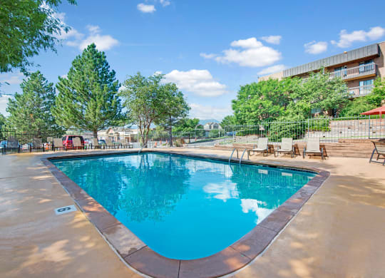 Outdoor swimming pool here at Eagle Ridge Apartment Homes surrounded by lounge chairs and trees, under a clear blue sky. The scene is peaceful and inviting, conveying relaxation.