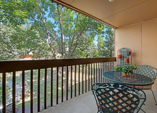 Cozy balcony here at Eagle Ridge Apartment Homes with metal table, chairs, and potted plants overlooking lush trees. Sunlight filters through branches, creating a serene atmosphere.
