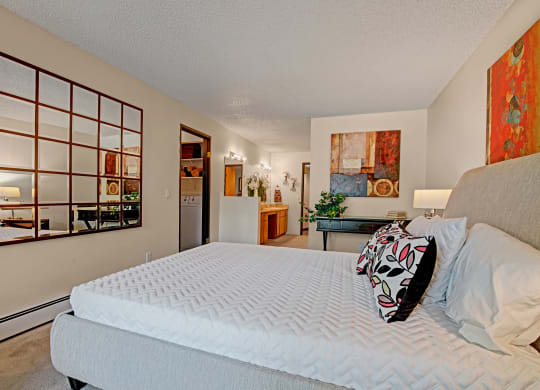 A modern bedroom here at Eagle Ridge Apartment Homes featuring a neatly made bed with floral pillows, a patterned wall mirror, abstract art, and gentle lighting, exuding a calm, stylish ambiance.