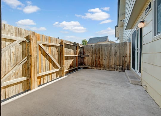Enclosed patio here at Yorkshire Square Apartment Homes with wooden fence, concrete floor, and sliding glass door. Bright, sunny day with blue skies and scattered clouds. Cozy, private vibe.
