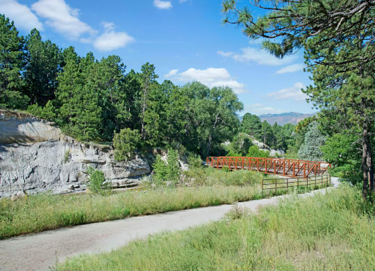 Wooden bridge near Yorkshire Square Apartment Homes over a lush green ravine, framed by rocky cliffs and dense trees under a clear blue sky. A peaceful and scenic landscape.