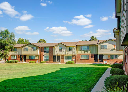 Row of two-story suburban Yorkshire Square Apartment Homes with a brick and siding exterior, set against a clear blue sky. Green lawn and trees create a serene atmosphere.