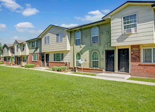 Row of modern Yorkshire Square Apartment Homes with varied facades, green lawns, and clear blue skies. The setting feels peaceful and suburban.