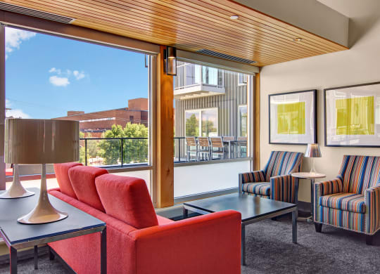 Modern lounge here at 7west Apartment Homes with a red sofa and striped armchairs near large windows. Bright, airy space features abstract art and a patio view. Cozy ambiance.