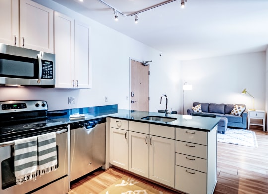 Stylish apartment here at 7west Apartment Homes with modern kitchen featuring stainless steel appliances and sleek counters, adjacent to a cozy living room with a blue sofa and accent lighting.