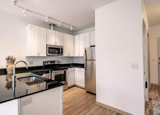 Modern kitchen here at 7west Apartment Homes with white cabinets, stainless steel appliances, and black countertops. Warm wood floors and soft lighting create a cozy, inviting feel.