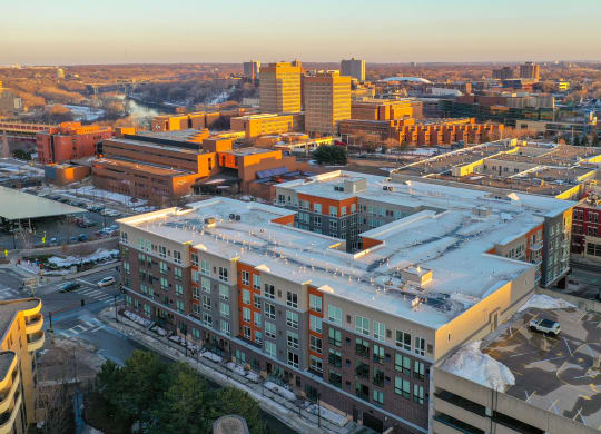 Aerial view of 7west Apartment Homes at sunset. Modern buildings with white and orange accents are prominent. Snow patches and trees are visible, conveying a calm winter scene.