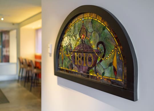 Stained glass artwork at 7west Apartment Homes with "1810" in purple, surrounded by ornate patterns and vibrant colors. It hangs on a softly lit wall, evoking elegance.