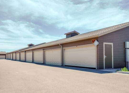 Row of beige garages here at Dakota Ridge Apartment Homes in a clean, empty lot under a clear blue sky. The scene is calm and orderly, with a modern, suburban feel.