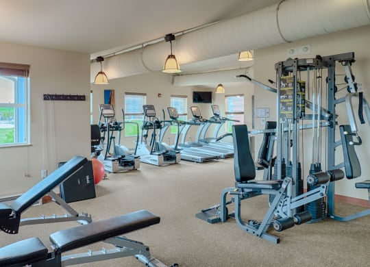 Bright, spacious gym here at Dakota Ridge Apartment Homes with modern equipment. Treadmills line the back wall near windows; a multi-gym machine and benches are in the foreground. Inviting atmosphere.