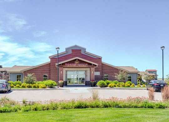 Red-brick Dakota Ridge Apartment Homes building under clear blue sky, with manicured shrubs and parked cars in front, conveying a welcoming and orderly atmosphere.