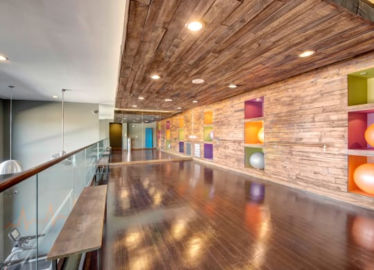 Stylish studio with polished floors here at the Enclave at Brookside Apartments, rustic wooden ceiling, colorful walls and recessed cubbies holding exercise balls, creating a vibrant, airy atmosphere.