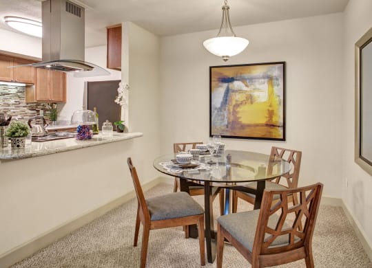 a dining area with a glass table and chairs and a kitchen in the background