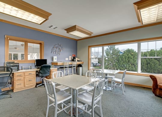 Bright business center at Arbor Ridge Apartments with blue walls features a computer desk, metal furniture, and a large window with trees outside, creating a calm, productive atmosphere.