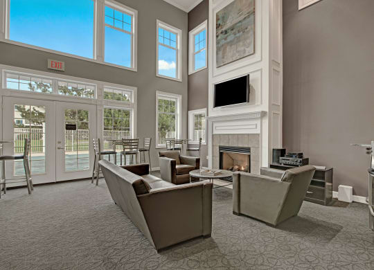 Bright, modern lounge at Arbor Ridge Apartments with large windows, gray sofas, a fireplace, and a wall-mounted TV. The mood is cozy and inviting, with natural light.
