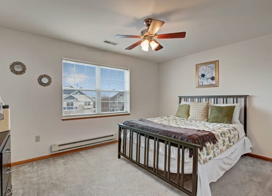 Bedroom with a metal-framed bed, floral bedding, and green pillows at Arbor Ridge Apartments. A ceiling fan, wall art, and two round mirrors enhance the cozy ambiance.
