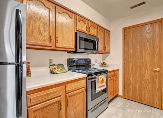 A modern kitchen with wooden cabinets, stainless steel appliances, and white countertops. A decorative towel hangs on the stove, adding a cozy touch. Arbor Ridge Apartments