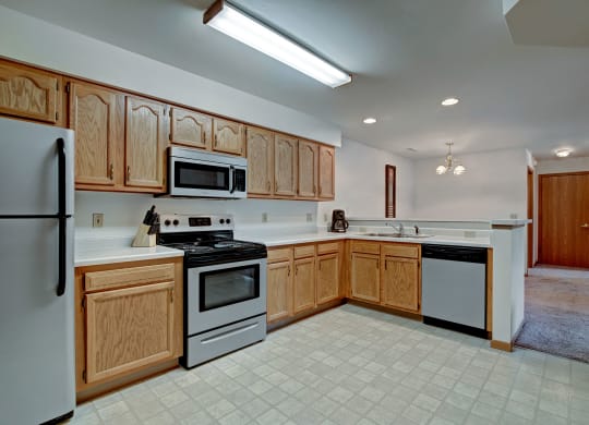 A spacious kitchen with wooden cabinets, stainless steel appliances, and tiled flooring. The room is well-lit, conveying a warm, inviting atmosphere. Arbor Ridge Apartments