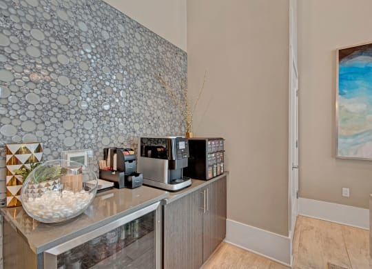 Stylish coffee station with a modern espresso machine, pods, and decor. Bubble-patterned backsplash; abstract blue art on the wall at River House Apartments.