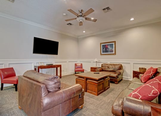 Cozy community lounge with brown leather sofas, red accent chairs, and decorative pillows. A large TV is mounted on the wall, and a coffee table sits centrally at St. James Apartments.