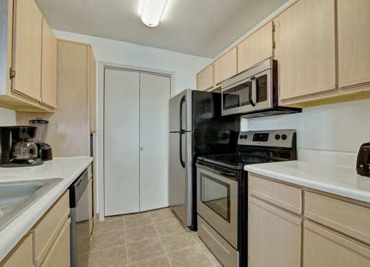 A modern kitchen with light wood cabinets, stainless steel appliances, and black accents. A coffee maker and toaster are on the counters at St. James Place Apartments.