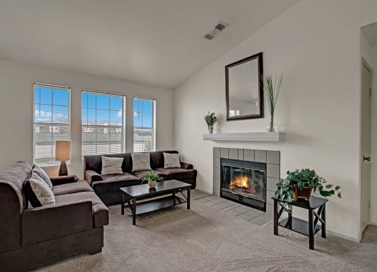 Cozy living room with brown sofas, a lit fireplace, and a mirror above the mantel. Large windows let in natural light at St. James Place Apartments.