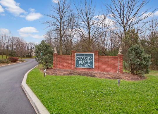 Entrance sign for St. James Place Apartments with a brick structure, surrounded by greenery and bare trees under a partly cloudy sky. Peaceful atmosphere.