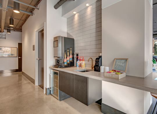 Modern coffee station with a sleek countertop, drink dispensers, flavor syrups, and a tea selection at Stitchweld Apartments.