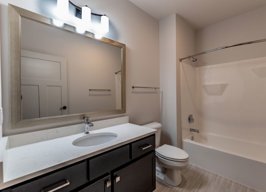 Modern bathroom at the Park Apartments with a clean, minimalistic design. Features include a large mirror, sleek vanity with a white countertop, and a bathtub with shower.