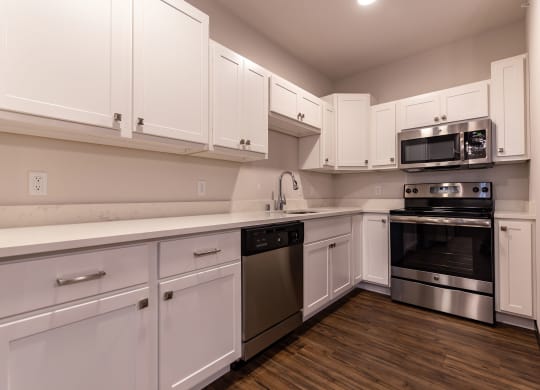 Modern kitchen at the Park Apartments with white cabinets, granite countertops, stainless steel appliances, and wood flooring. The space is clean and well-lit.
