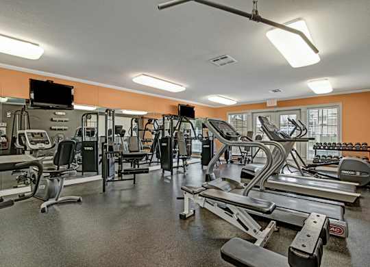 A gym with a variety of equipment including treadmills, weights, and exercise machines.
