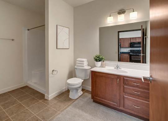 A clean bathroom here at Latitude featuring a spacious vanity with warm wood cabinetry, bright lighting, and a walk-in shower, creating a fresh, open, and welcoming space.