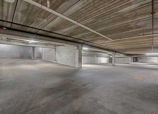 A spacious underground parking garage here at Latitude featuring wide concrete drive lanes, sturdy support columns, and bright overhead lighting, creating a convenient and secure area for resident parking.