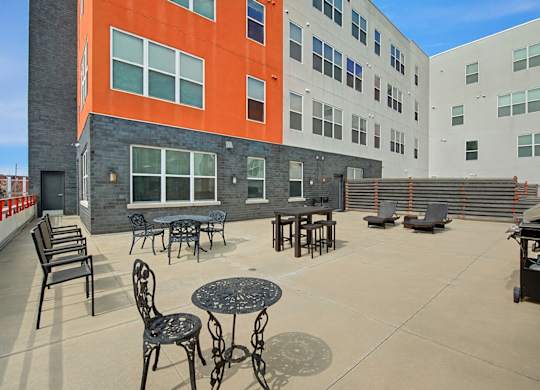 A spacious outdoor patio here at Latitude featuring stylish seating areas, café tables, lounge chairs, and grilling space, creating a bright and inviting setting for relaxing and socializing.