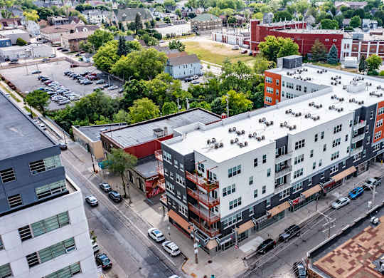 An aerial exterior view here at Latitude showcasing a modern apartment community with gray and orange accents, street-level retail, and a vibrant neighborhood setting surrounded by trees and city streets.