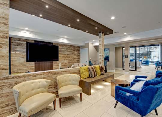 A modern clubhouse space here at River House featuring white and blue comfortable sofas, a large flatscreen tv, and bright lights giving the space an open, cozy, and welcoming feel for residents.