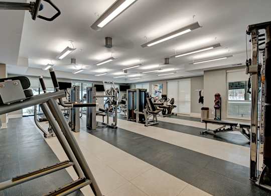 A modern fitness center here at River House including several exercise equipment, bright lights, and large windows, creating a motivating workout envrionment,