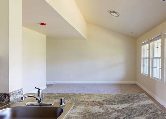 A bright living room here at St. James Place with soft beige carpet, cream walls, and large windows that bring in natural light. A breakfast bar overlooks the space, creating an open and inviting layout.