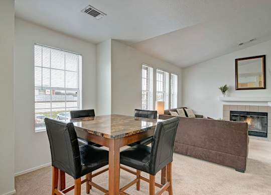 A bright dining area here at St. James Place with soft beige carpet, large windows, and a modern dining table. A nearby fireplace and open living space create a warm and inviting atmosphere.